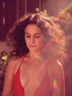 a woman in a red swimsuit standing next to some bushes and flowers with her eyes closed