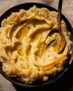 mashed potatoes with butter and herbs in a black bowl on a white tablecloth