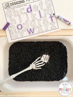 a tray with black beans and a white plastic fork in it, next to a printable alphabet