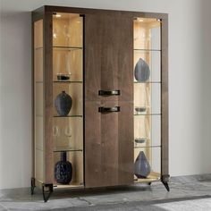 a wooden cabinet with glass doors and vases on the bottom shelf next to it