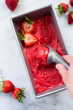 someone is scooping strawberries into a metal container with ice cream on the table