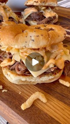 two sandwiches with meat and cheese on them sitting on a cutting board next to chips