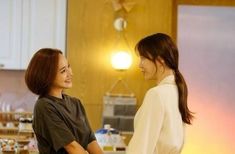 two young women standing in a kitchen talking to each other and smiling at one another