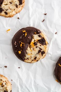 three cookies with chocolate and orange peels on white parchment paper, one half eaten