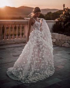 a woman in a wedding dress standing on a balcony with the sun setting behind her