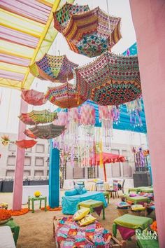 many colorful umbrellas hanging from the ceiling in an open area with tables and chairs