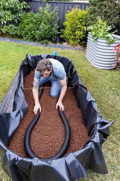 a man is using a vacuum to clean the soil in his garden bed with a hose