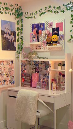 a white desk topped with a computer monitor next to a wall covered in pictures and plants