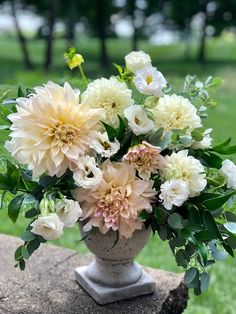 a vase filled with lots of flowers sitting on top of a stone slab in the grass