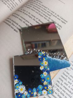 two pieces of glass with daisies on them sitting on top of an open book