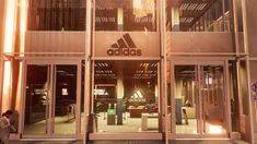 the adidas storefront is lit up at night with people walking in and out