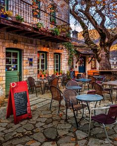 tables and chairs in front of an old building with a chalkboard sign on it