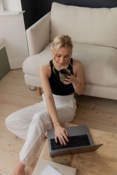 a woman sitting on the floor with her laptop and cell phone in front of her