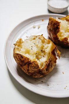 two baked potatoes on a plate with butter and seasoning sprinkled on them