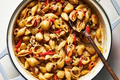 a skillet filled with pasta and meat on top of a white counter next to a wooden spoon