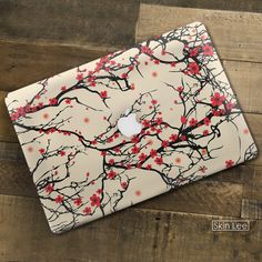 an apple laptop computer sitting on top of a wooden table covered in red and black flowers