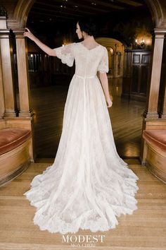 a woman in a white wedding dress standing on a wooden floor with her arms outstretched