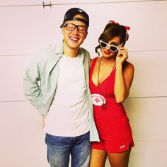 a man standing next to a woman in a short red dress and hat while talking on a cell phone