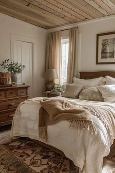 a large bed sitting under a window in a bedroom next to a dresser and lamp