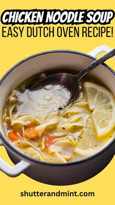 chicken noodle soup in a pot with lemons and carrots on the side