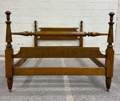 an antique wooden bed frame with four posts and headboard turned to the side, in front of a white brick wall