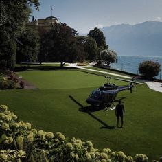 a helicopter parked on top of a lush green field next to the ocean with mountains in the background