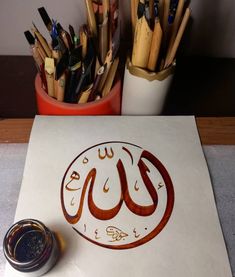 an arabic calligraphy is displayed on a table with pens and pencils in front of it