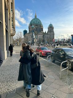 two people walking down the street in front of a large building