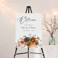 an easel holding a welcome sign with flowers on it and lights in the background