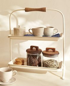 three tiered rack with cups and cookies on it next to a coffee cup, saucer and spoon