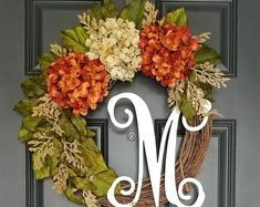 a wreath with the letter m on it and flowers hanging from it's front door