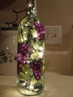 a glass bottle with flowers painted on it sitting on a counter next to a light switch