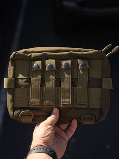 a hand holding an army style pouch with multiple compartments and two small eyes on it