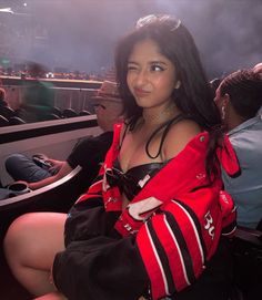 a woman sitting in the stands at a baseball game wearing a red and black jacket