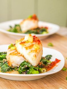 two white plates filled with food on top of a wooden table next to green vegetables