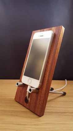 an iphone is plugged in to a charging station on a wooden table with a black wall behind it