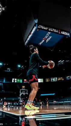 a woman in black shirt and shorts holding a basketball on top of a wooden court