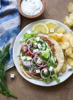 a white plate topped with a pita sandwich next to potato wedges and salad