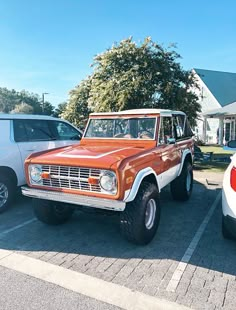 an orange and white truck parked in a parking lot next to other cars on the street