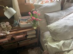 a bed with white sheets and pink tulips in a vase on the end table