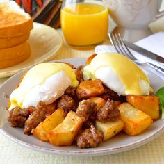 a white plate topped with eggs and meat covered in cheese next to toasted bread