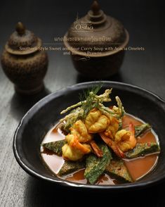 a black bowl filled with food on top of a wooden table next to a teapot