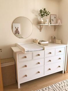 a white dresser sitting in a bedroom next to a mirror and shelf with pictures on it