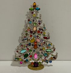 a christmas tree made out of jeweled stones on a white surface with a gold base