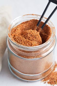 two spoons sticking out of a jar filled with ground spices and seasoning on a white surface