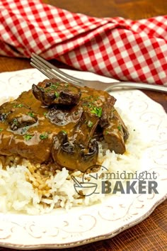 a white plate topped with rice and meat covered in gravy next to a fork