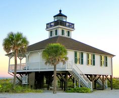 a white building with green shutters and a light house on top next to palm trees