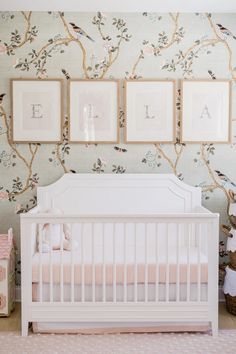 a white crib in front of a wall with pictures on it and framed photos above the crib