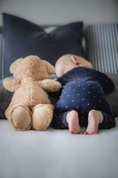 a baby sleeping next to a teddy bear on top of a bed with black pillows