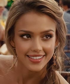 a close up of a person wearing earrings and smiling at the camera with other people in the background